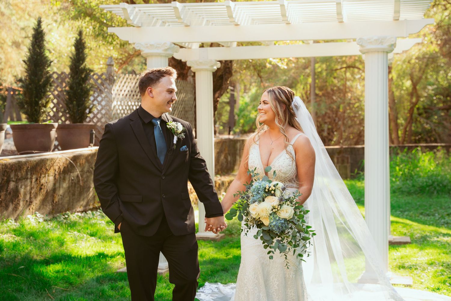 Wedding celebration under a white pergola with sunlit garden background.