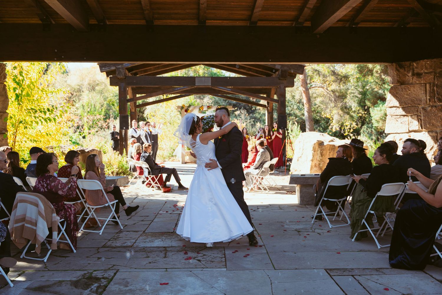 Panoramic view of an outdoor wedding venue with stone columns and wooden beams overhead.