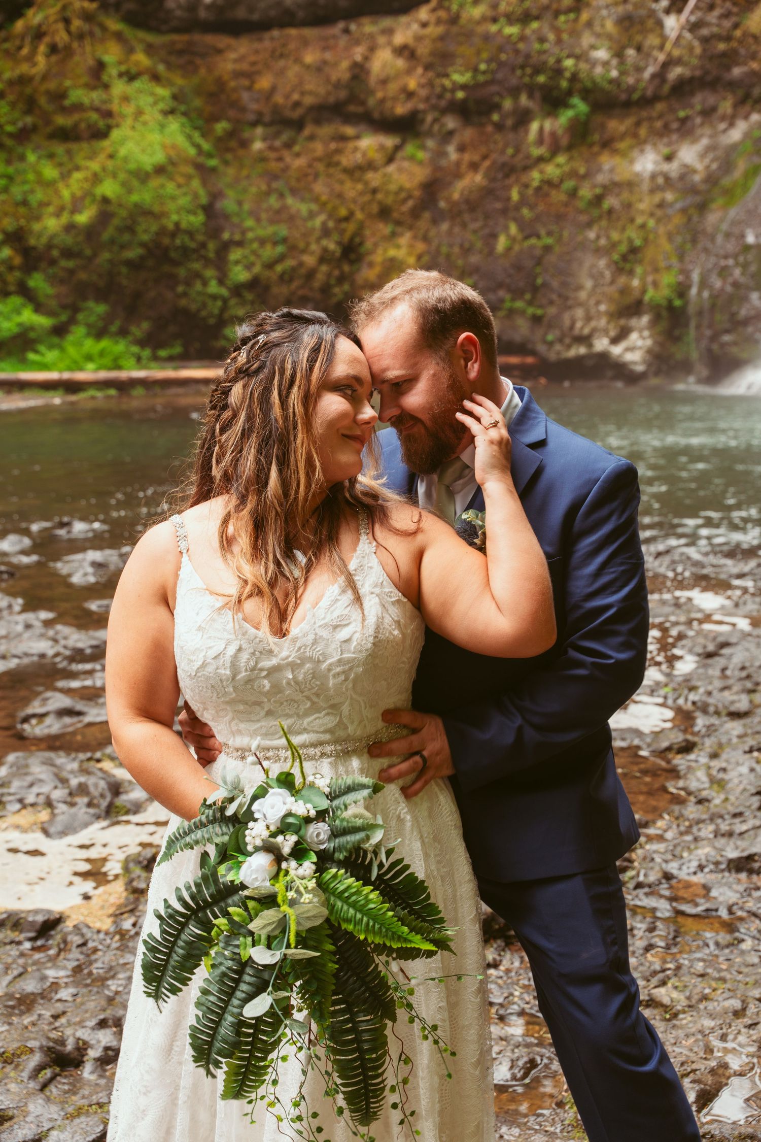 Couple embraces during their wedding photos with a cascading waterfall in the background.