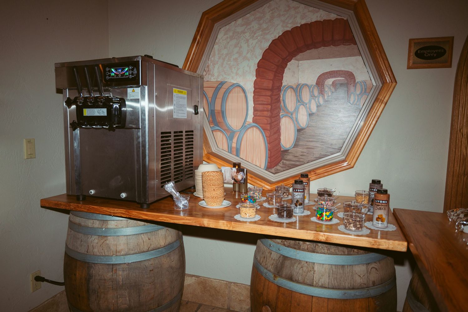 Rustic wine bar setup with wooden barrels and vintage equipment against a painted wall mural.