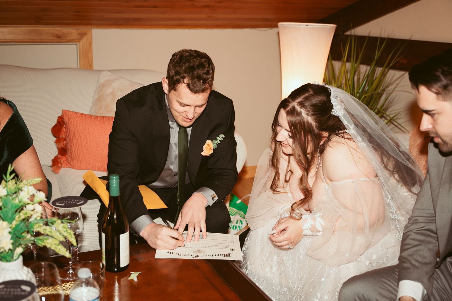 Wedding guests signing documents at wooden table during indoor reception.