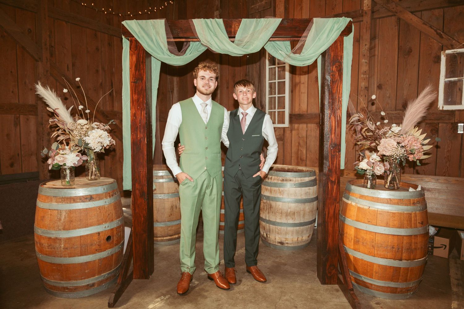 Wedding party poses between wooden barrels in a rustic barn setting with mint green accents.