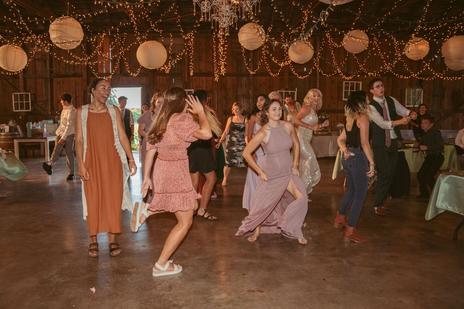 Dancers move across a barn dance floor decorated with string lights and paper lanterns.