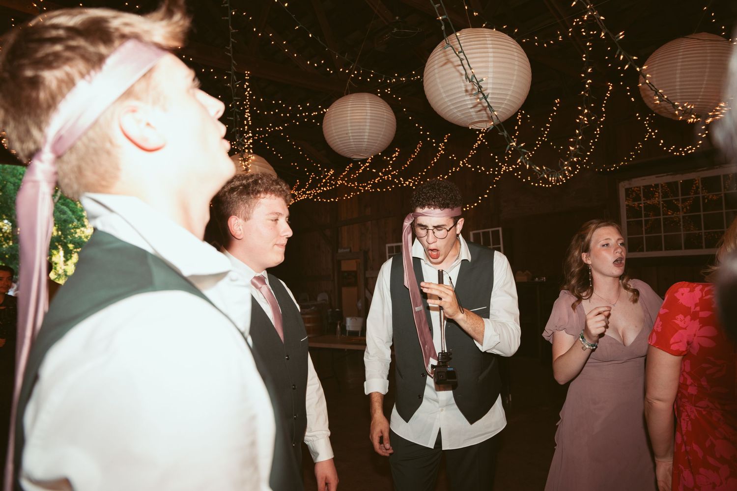 Wedding party dancing and celebrating in a barn venue with twinkling lights overhead.