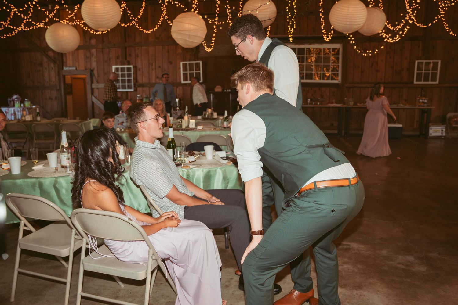 Wedding guests relax at tables while others dance under glowing string lights and paper lanterns.
