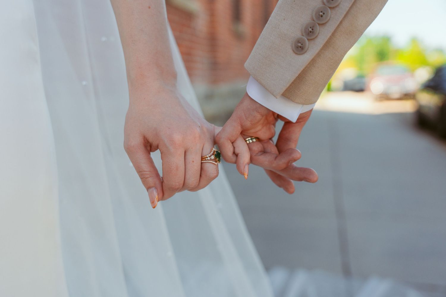 A close-up detail shot of wedding rings and intertwined hands in natural light.