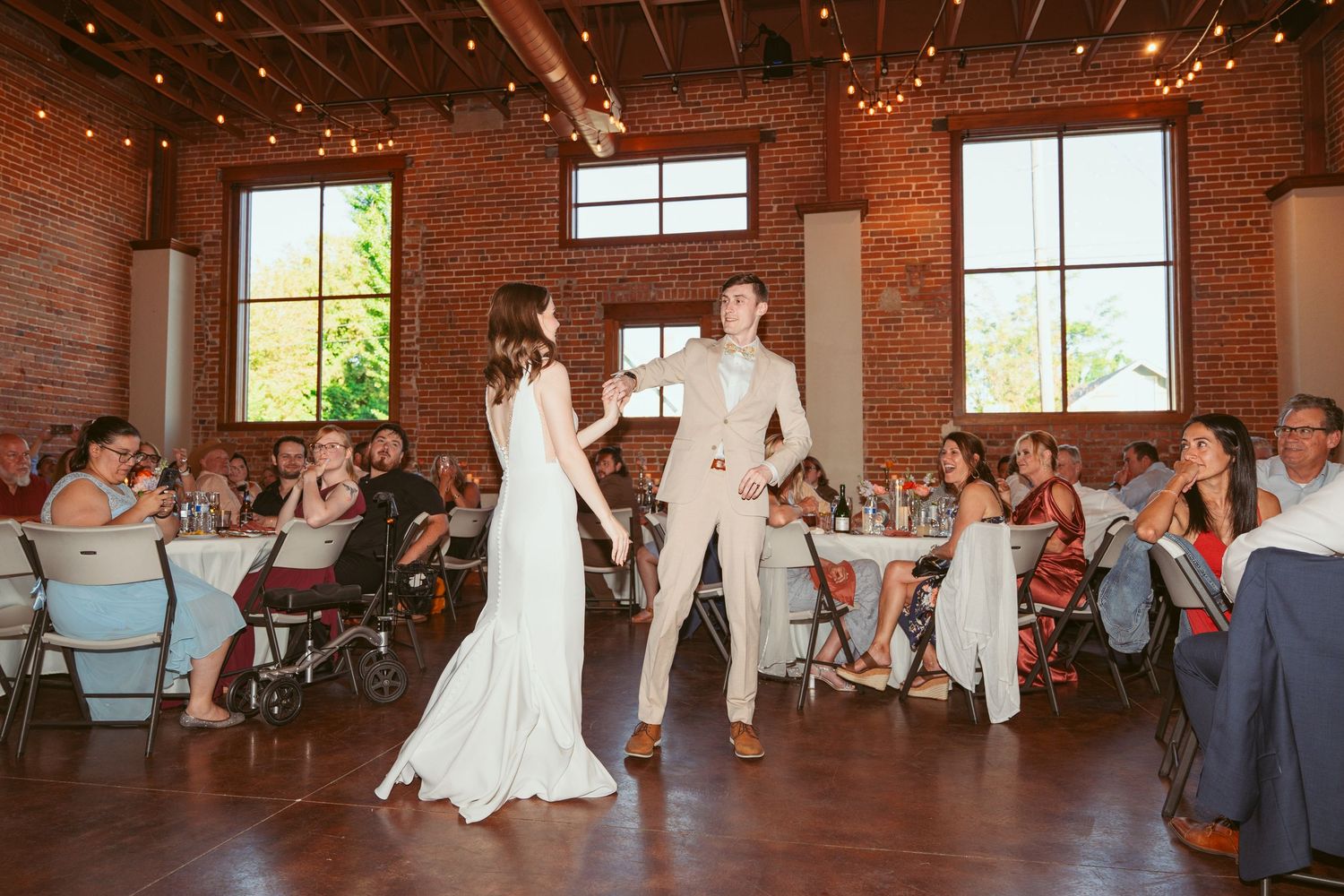 Newlyweds share intimate dance moment in industrial-style reception venue with exposed brick walls.