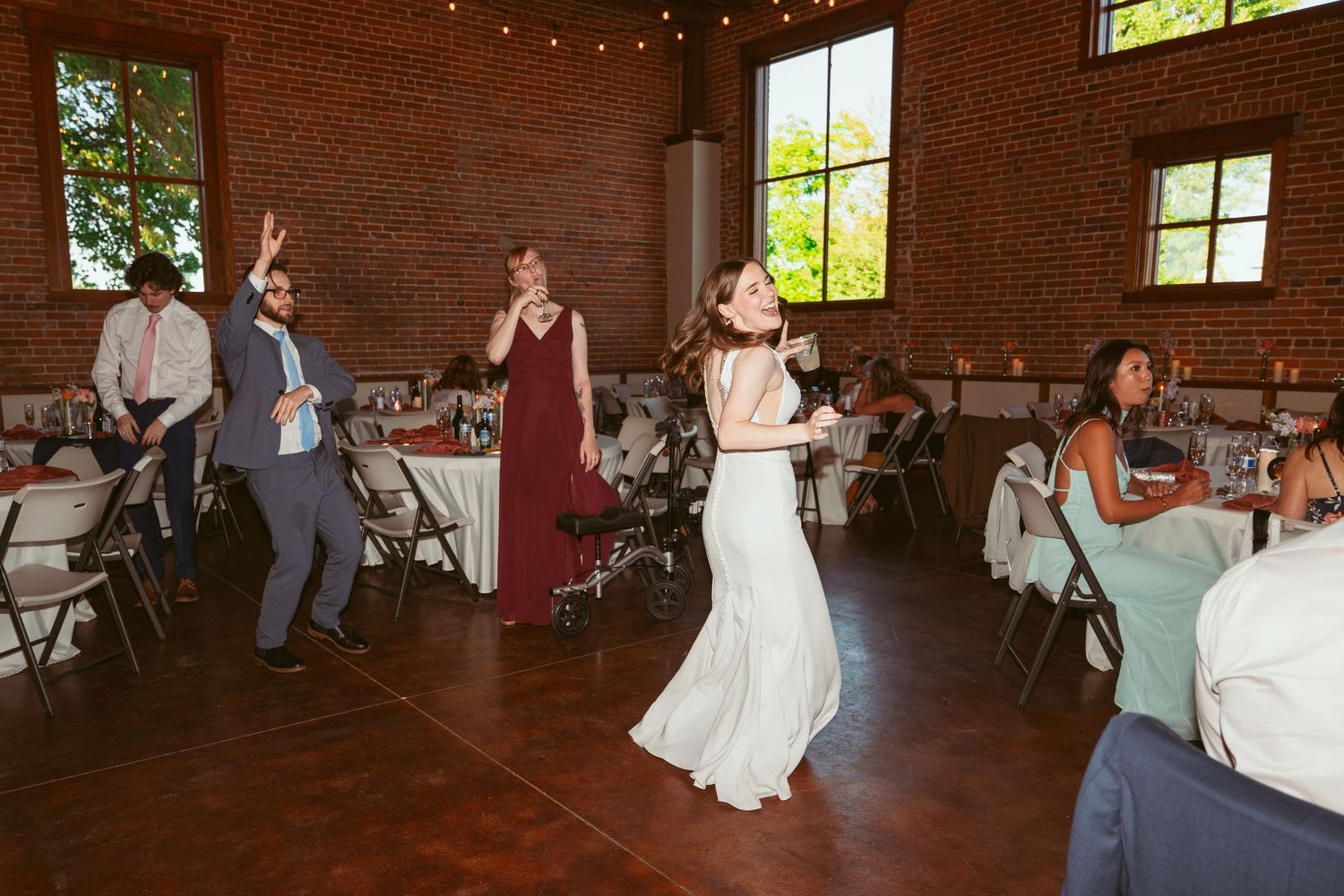Celebration on the dance floor with guests dancing in a historic brick venue with string lights.