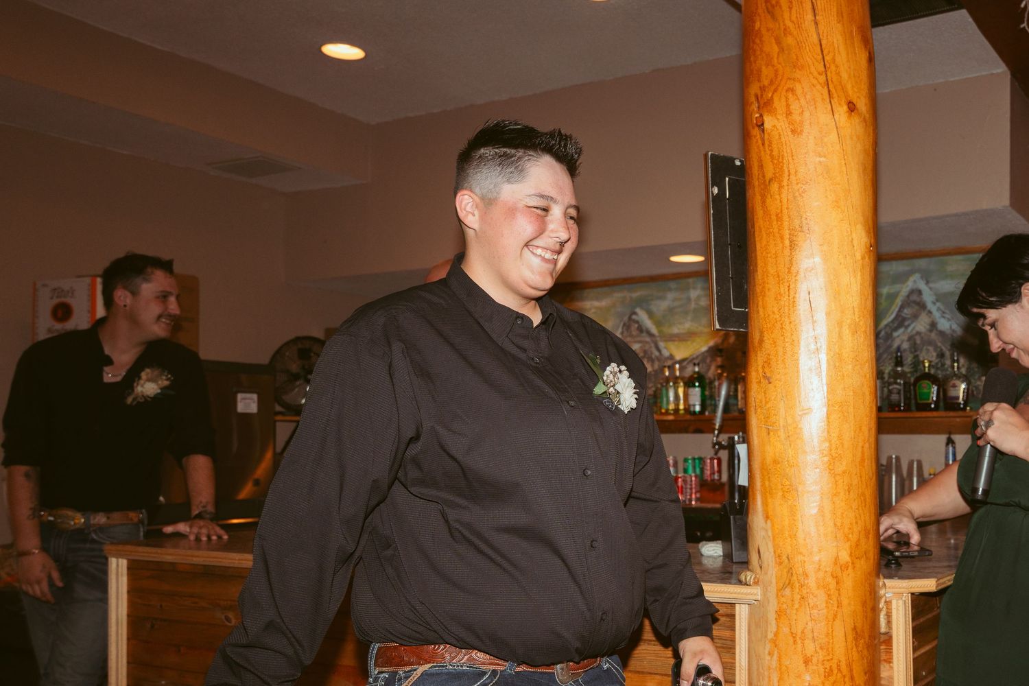 A person in black chef attire stands near a wooden post in an indoor restaurant setting.