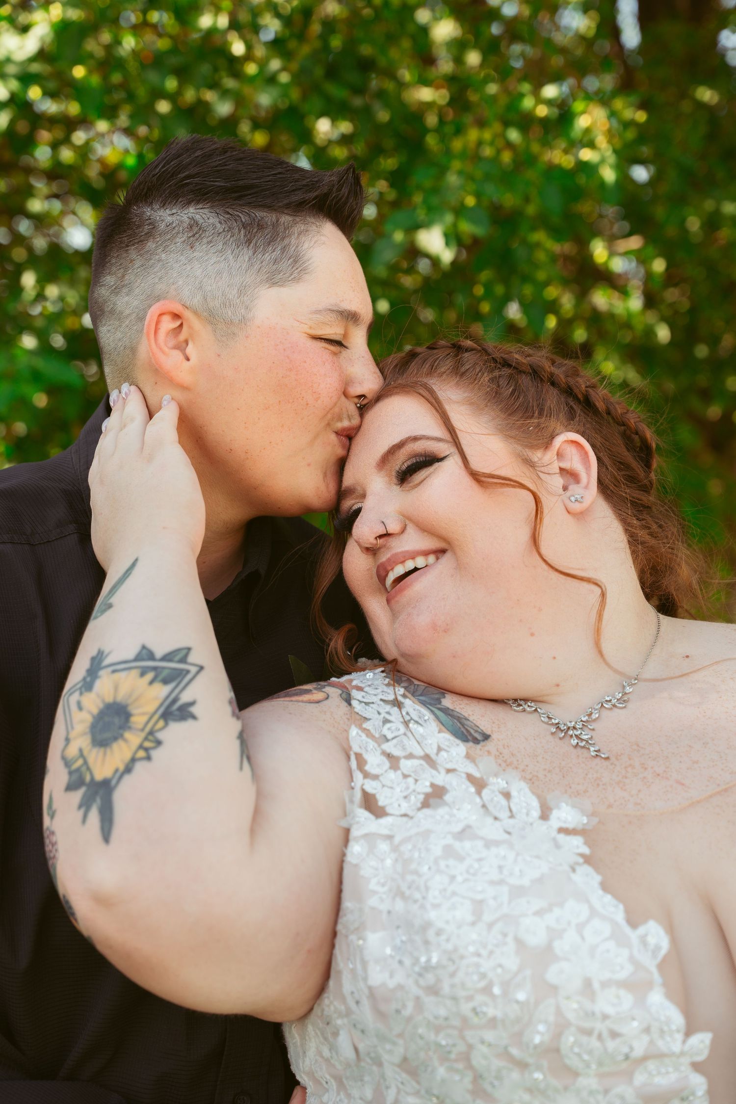 A romantic wedding portrait showing a tender moment between newlyweds against a green outdoor background.