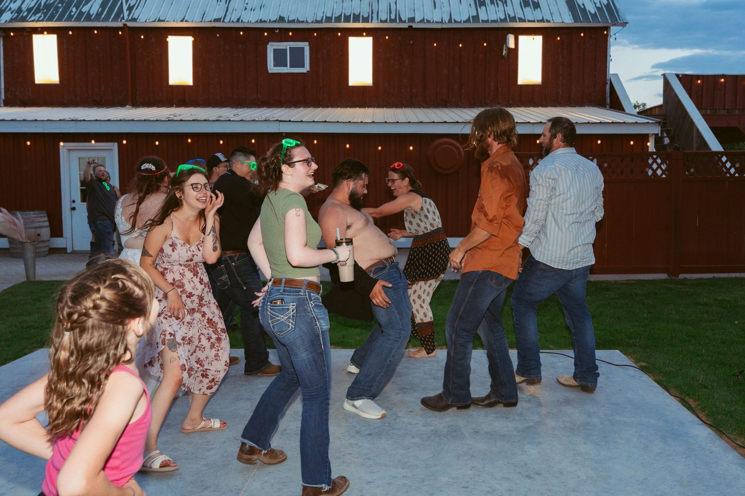 Evening wedding reception with guests dancing outdoors near a rustic barn venue.