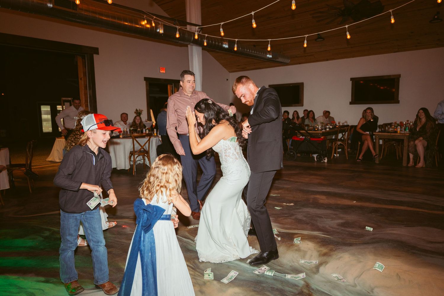 Wedding reception dance floor with string lights and exposed wooden beams overhead.