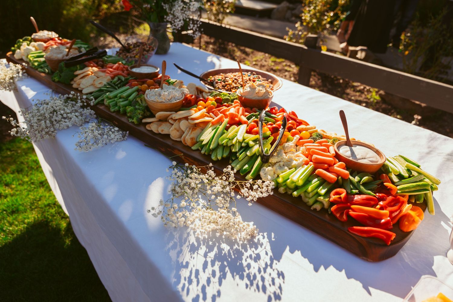 Fresh vegetable crudité platter with colorful bell peppers and dips on outdoor buffet table.