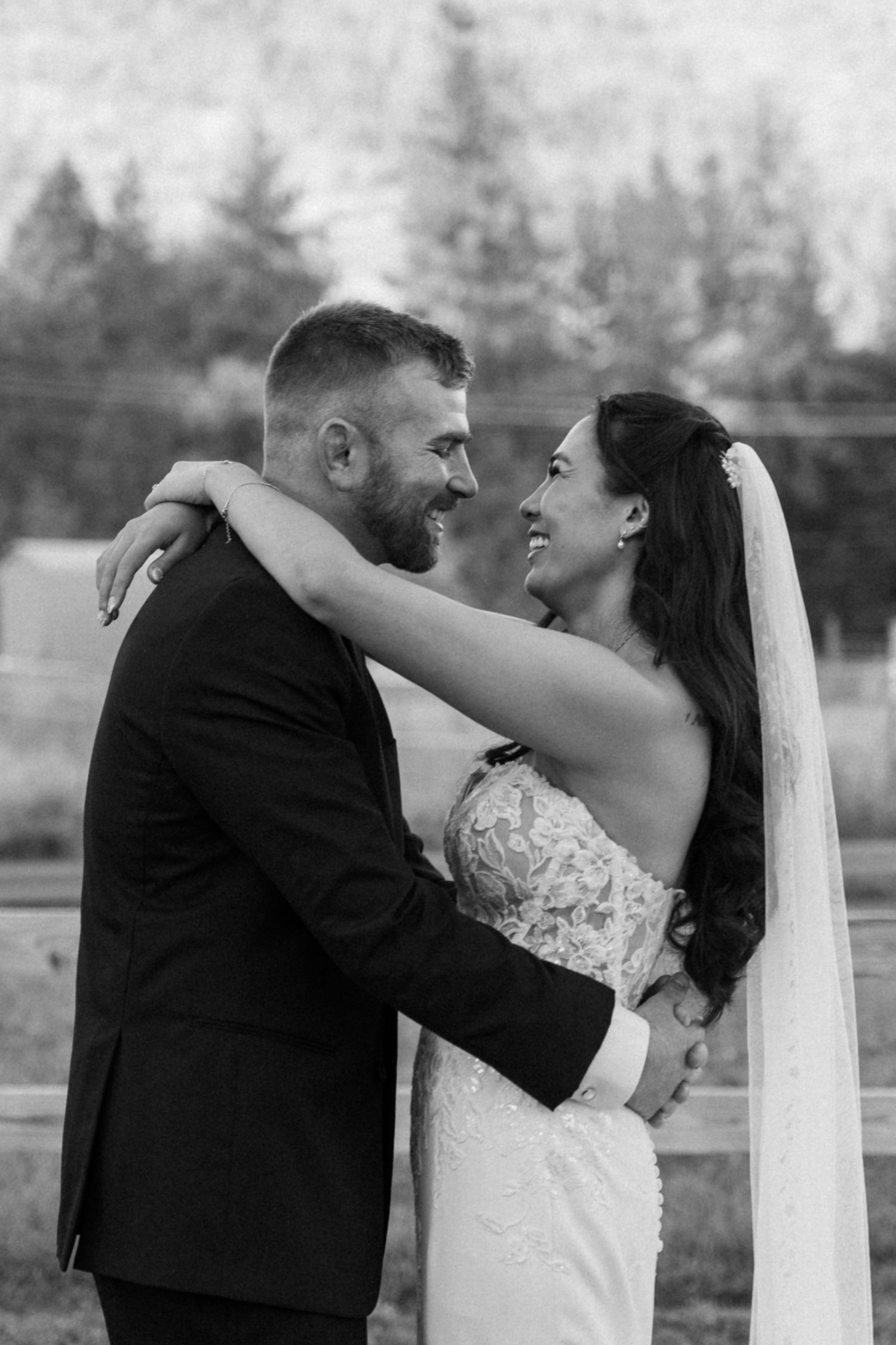 Black and white wedding photo showing tender moments between newlyweds outdoors.