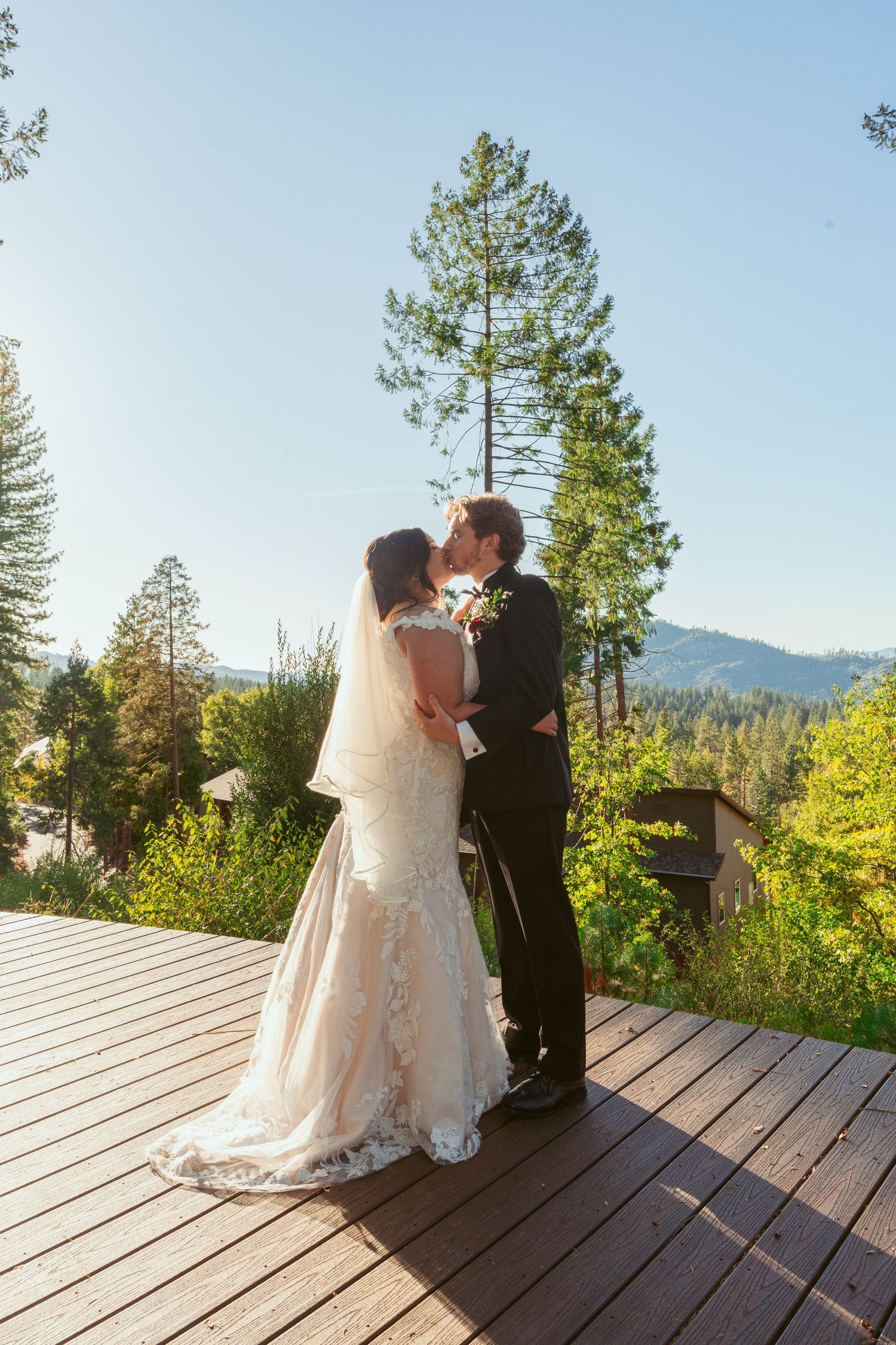 A couple shares their first kiss as newlyweds on a scenic mountain deck.