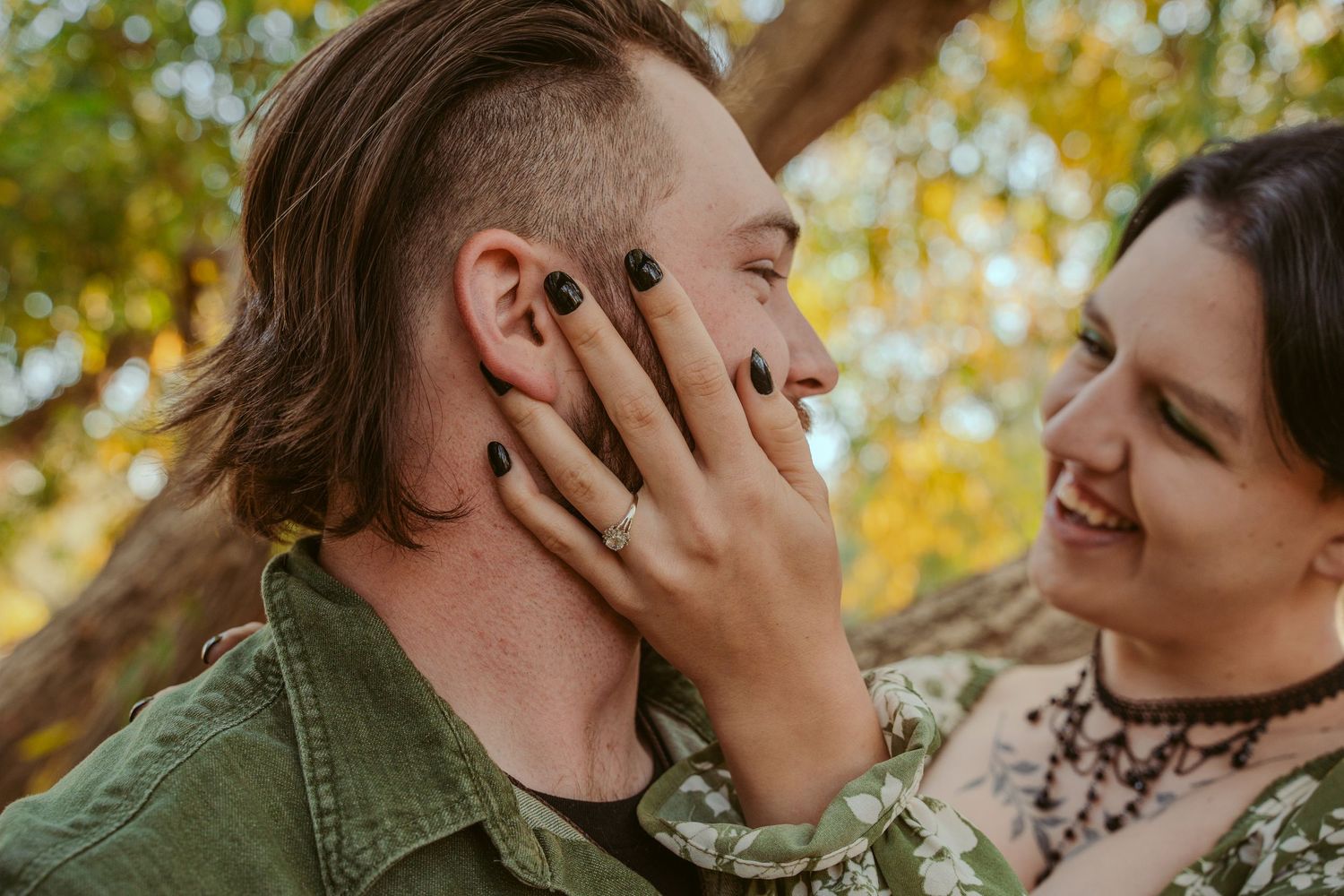 A couple shares a tender moment outdoors with golden autumn foliage in background.