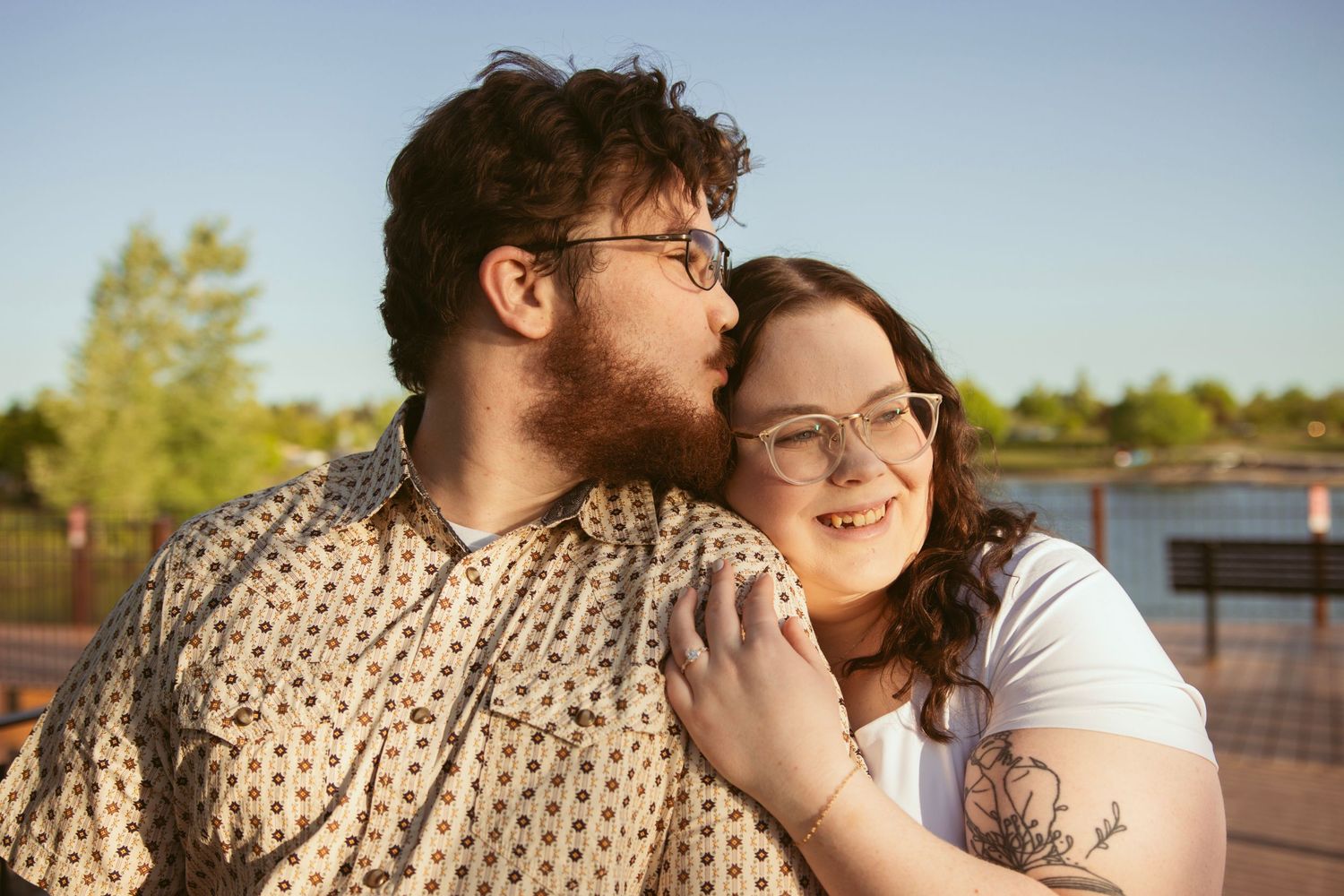 Tender moment shared between couple sitting by a serene lake during sunset.