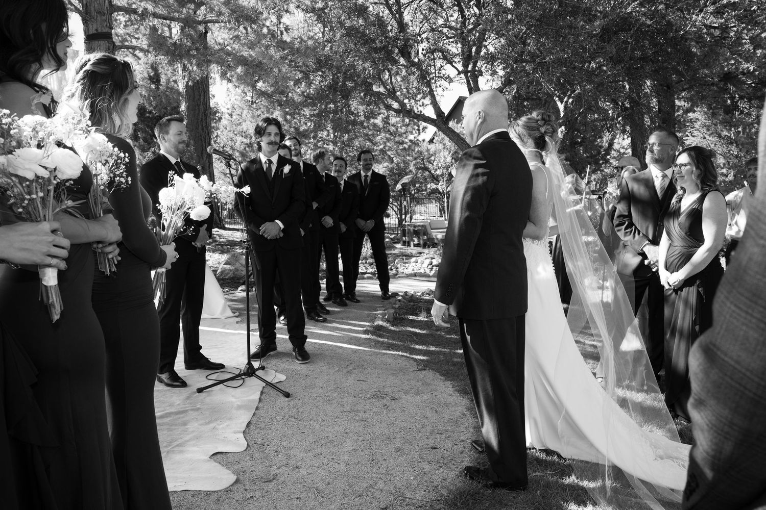 Black and white photo showing wedding guests and wedding party during an outdoor forest ceremony.