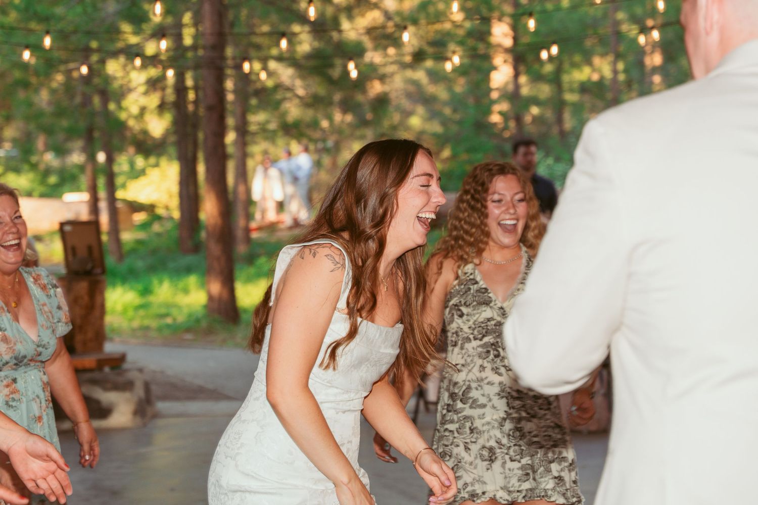 Wedding guests dancing in pairs during an evening celebration under a wooden pavilion.