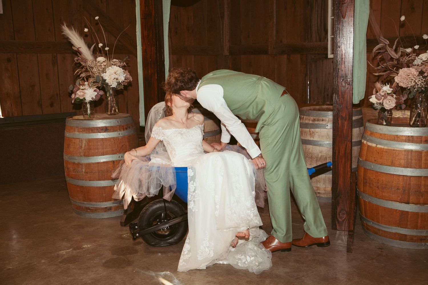 Wedding celebration with a playful moment near wooden barrels at a rustic venue.