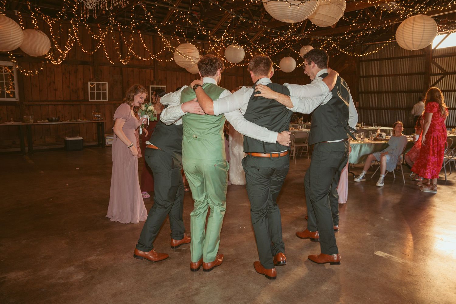 Guests perform a synchronized dance routine at a barn wedding reception under glowing lights.