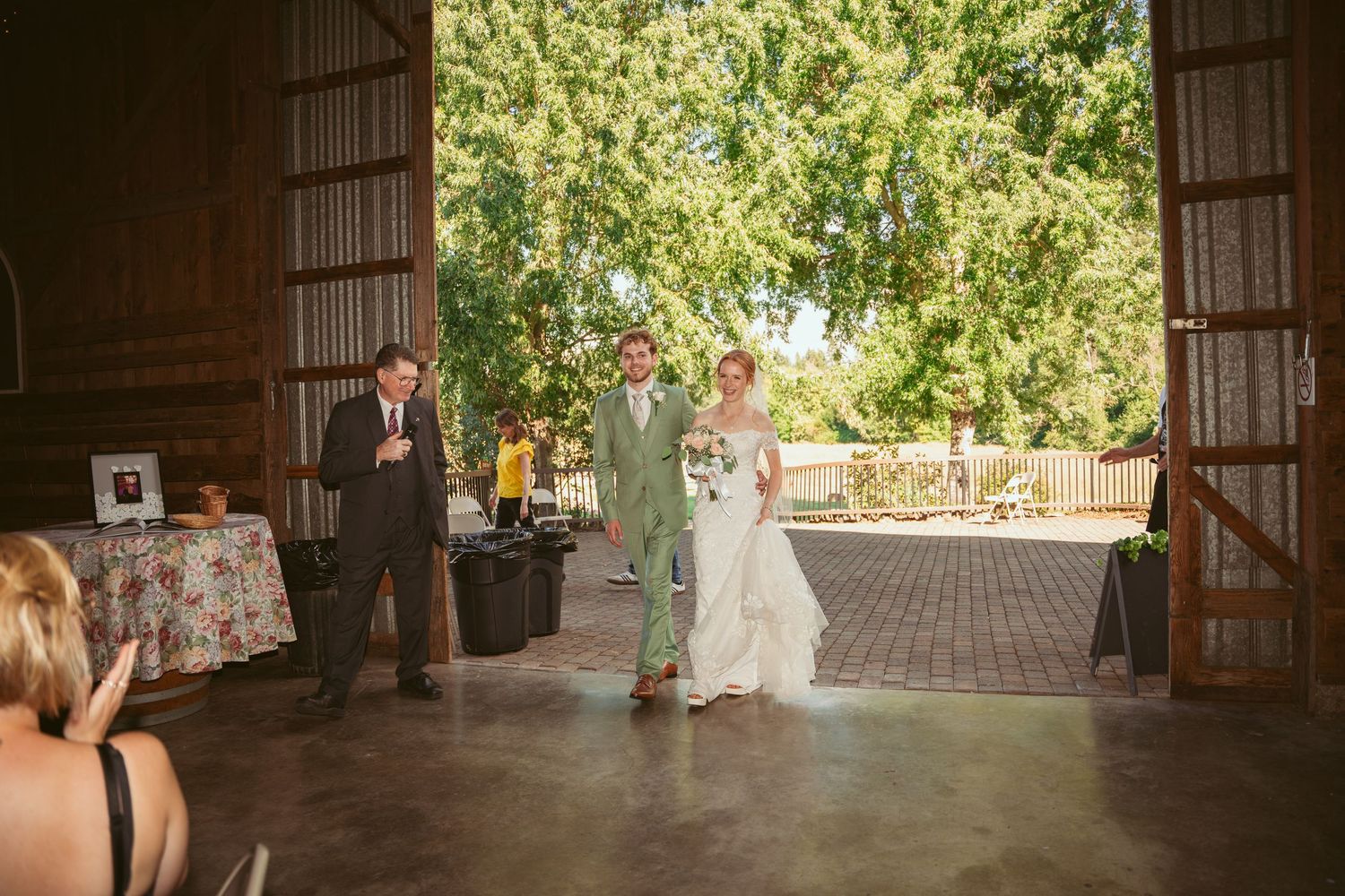 Sunlit barn interior with wooden beams and decorative lighting for a wedding reception.
