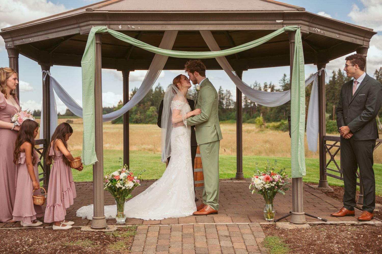 Outdoor wedding pavilion decorated with white fabric and pink flowers against a blue sky.
