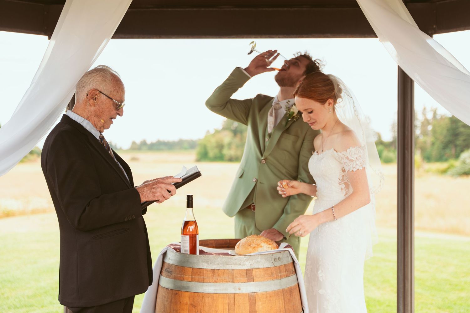 Wedding ceremony moment with couple and officiant around wooden barrel under gazebo.