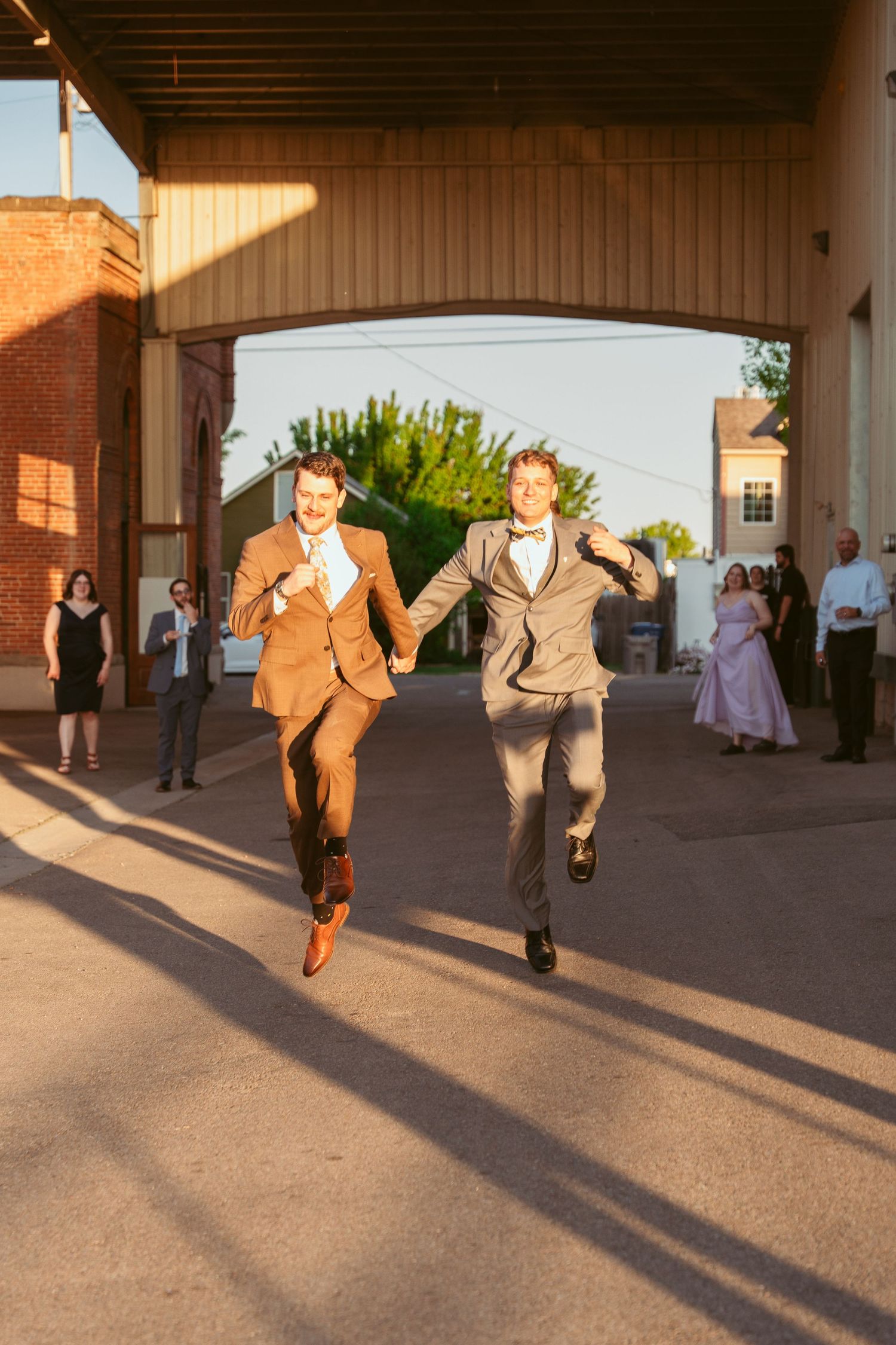 Groomsmen running in sequence at sunset creating long shadows on concrete.