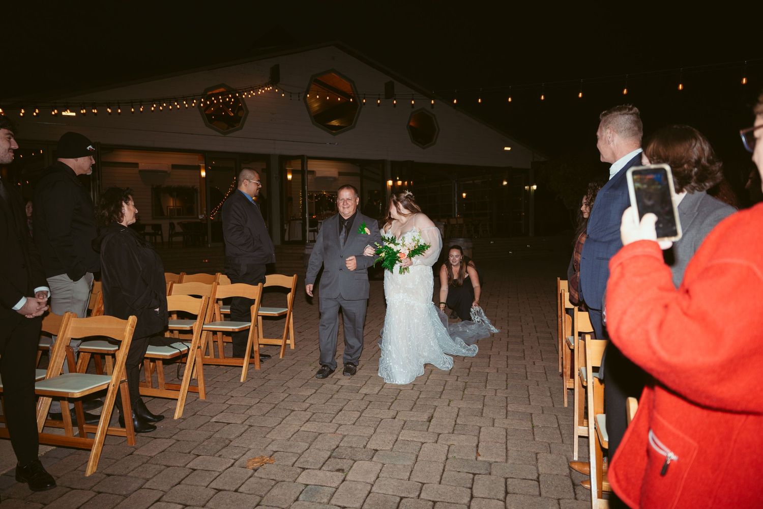 Wedding reception setup with wooden chairs and string lights at night.