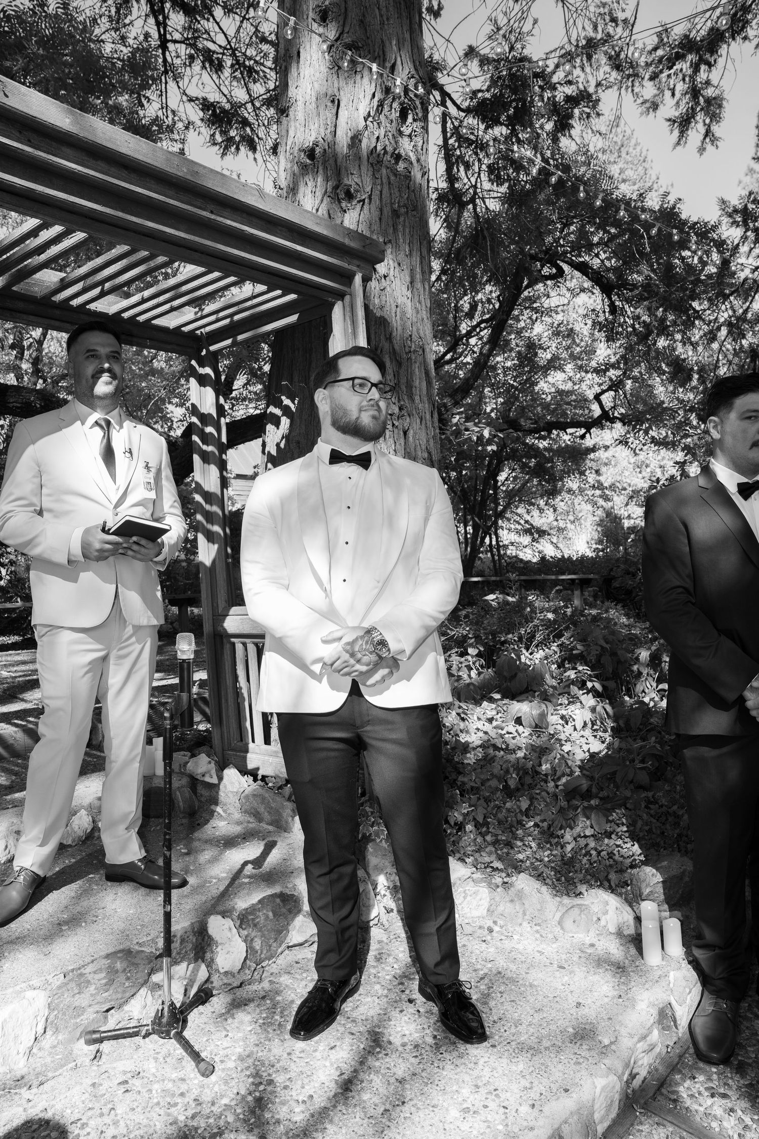 Groomsmen in white tuxedo jackets and black pants pose together in an outdoor garden setting.