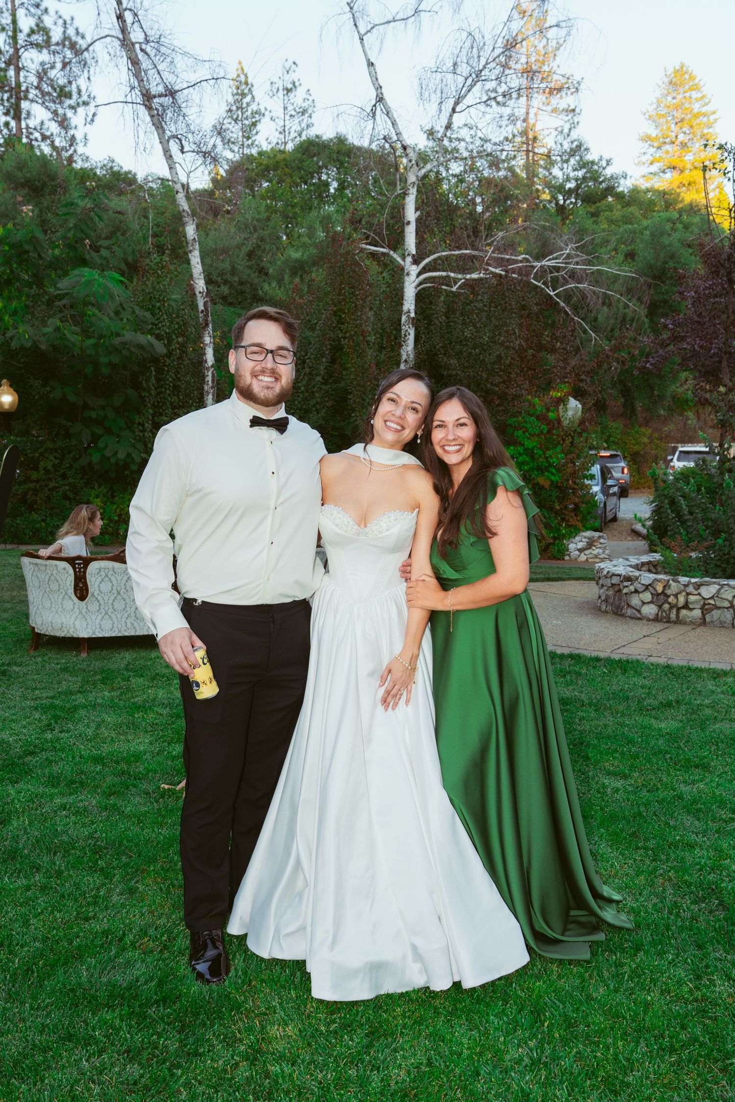Wedding party poses on grass with bride in white gown and attendant in emerald green dress.