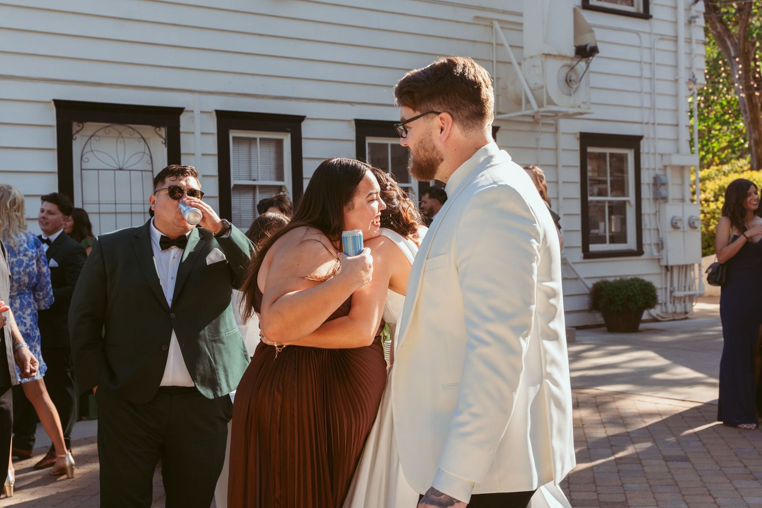Wedding guests mingling and socializing outside a white clapboard house on a sunny day.