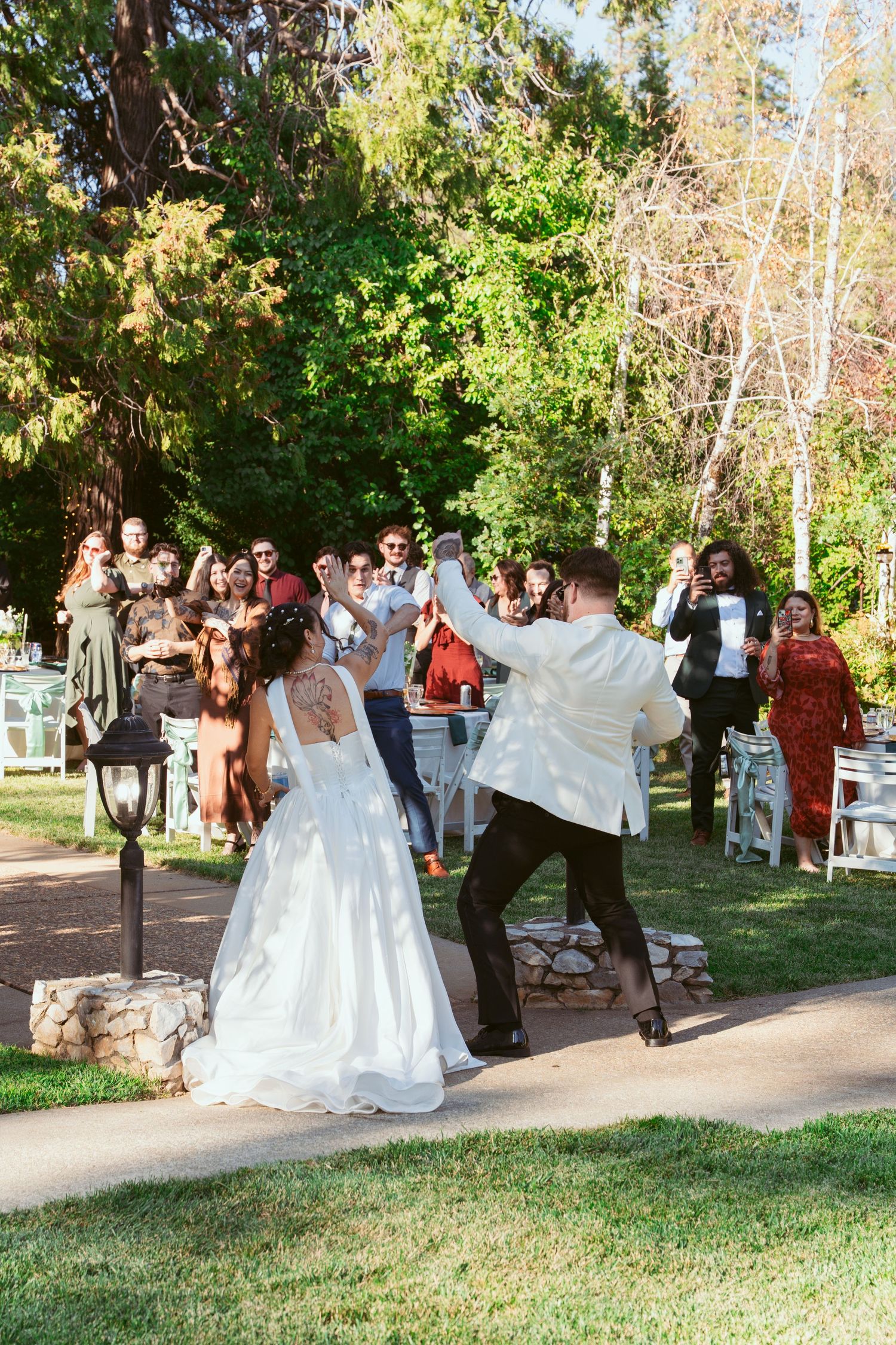 Wedding celebration in a sunny park with guests watching a couple in formal attire.