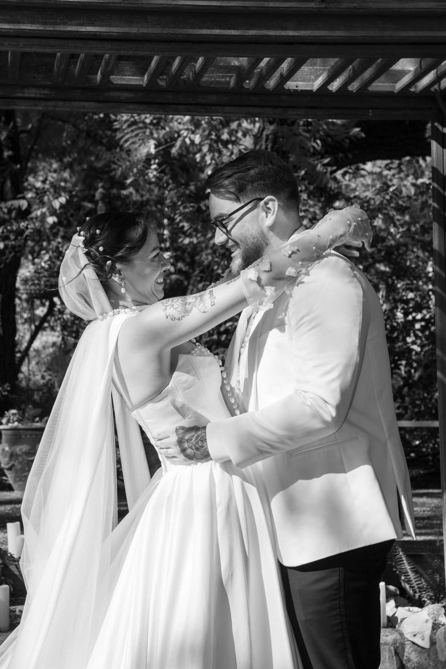 A tender moment between a couple during their wedding ceremony under a wooden pergola in black and white.