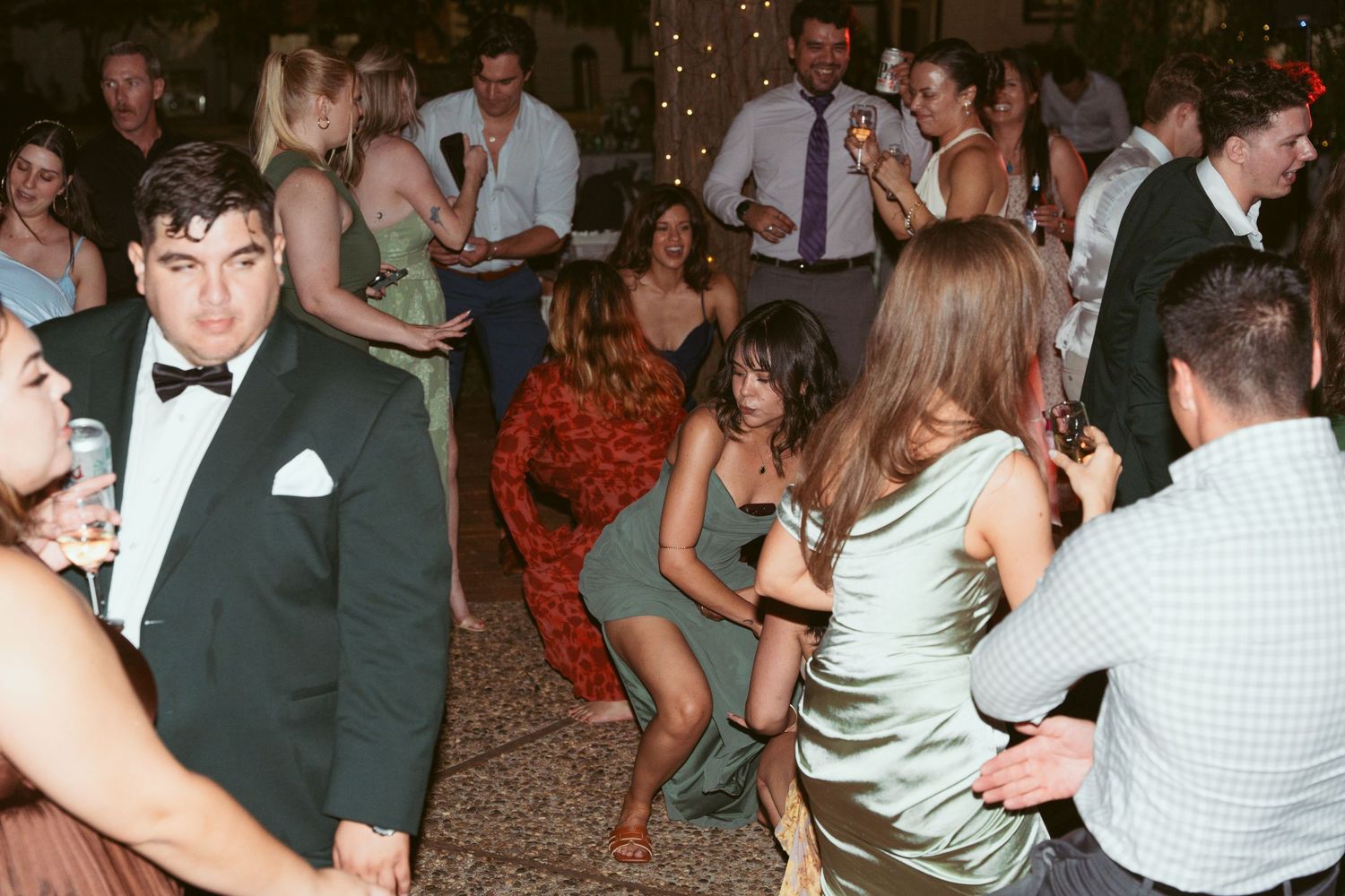 Couples dance and mingle at a festive outdoor wedding reception with string lights overhead.