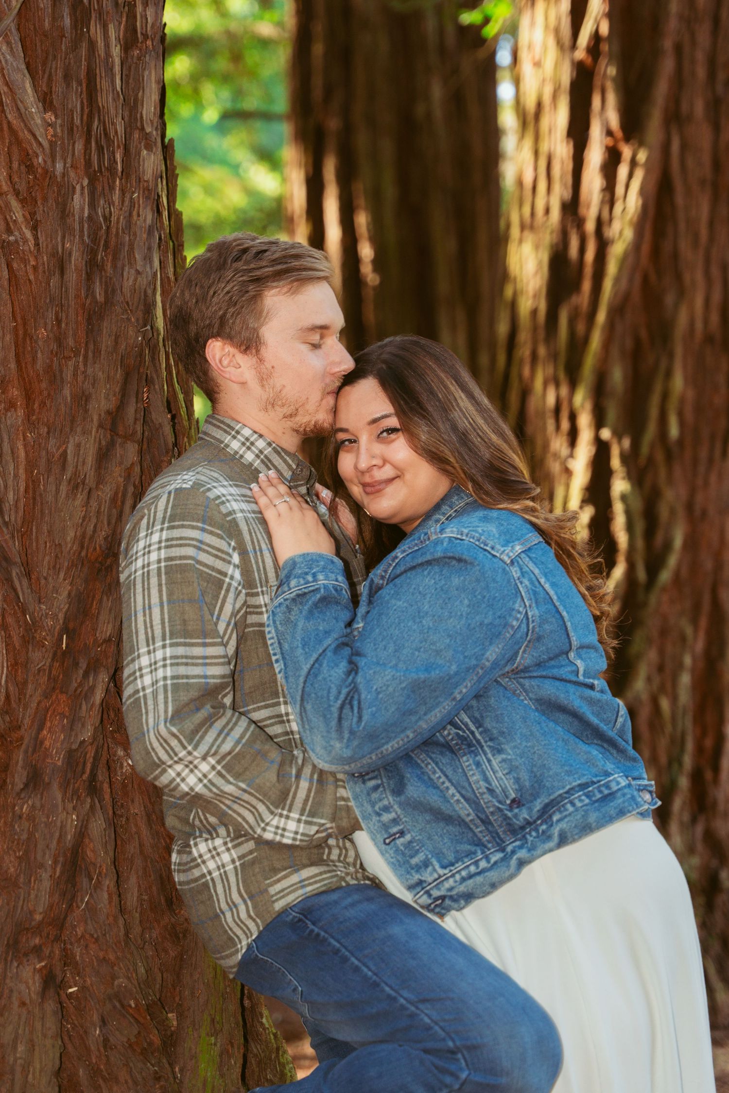Intimate embrace shared between two people against the backdrop of majestic redwood trees.