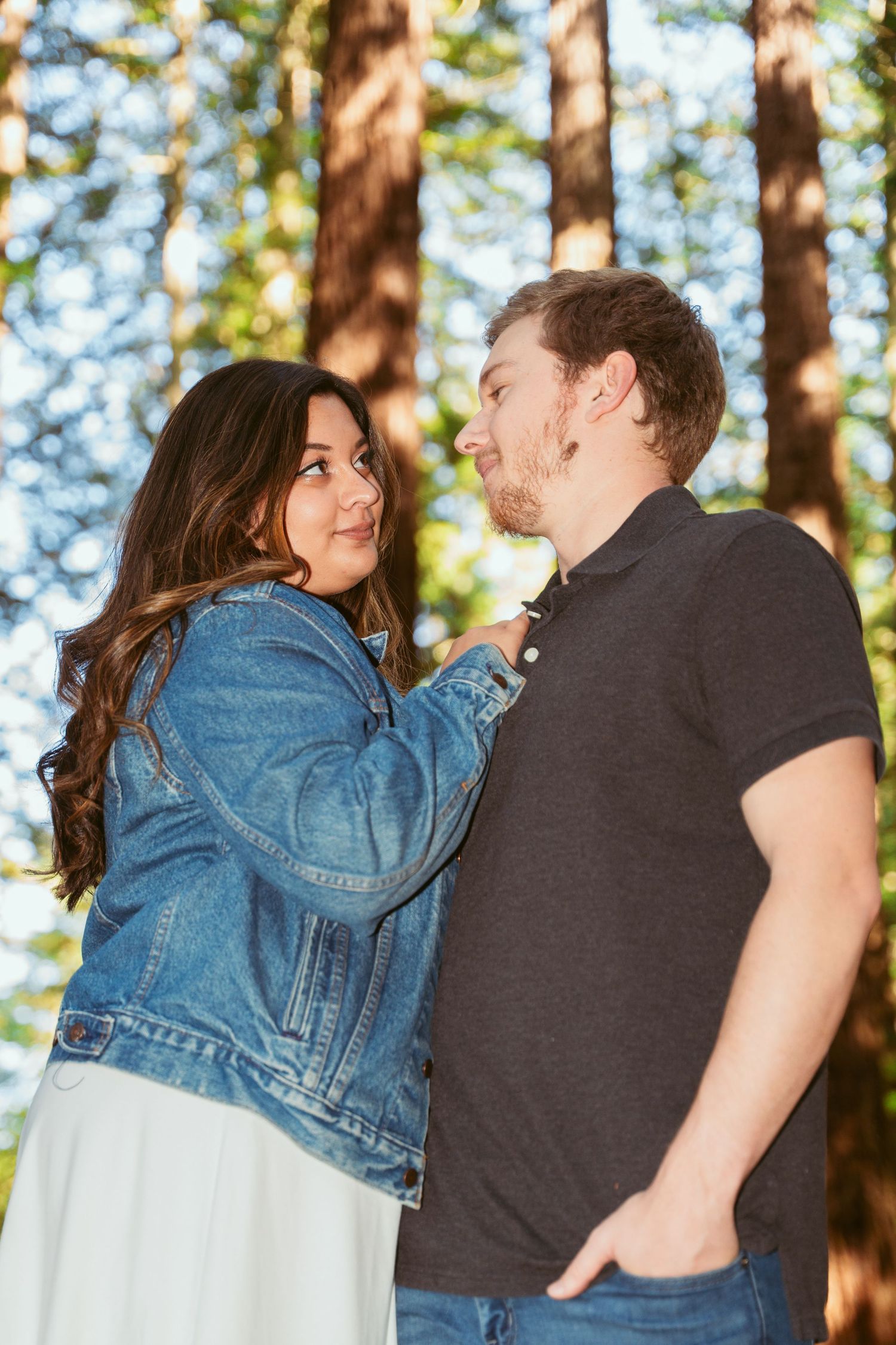 Candid romantic interaction between couple against forest backdrop.