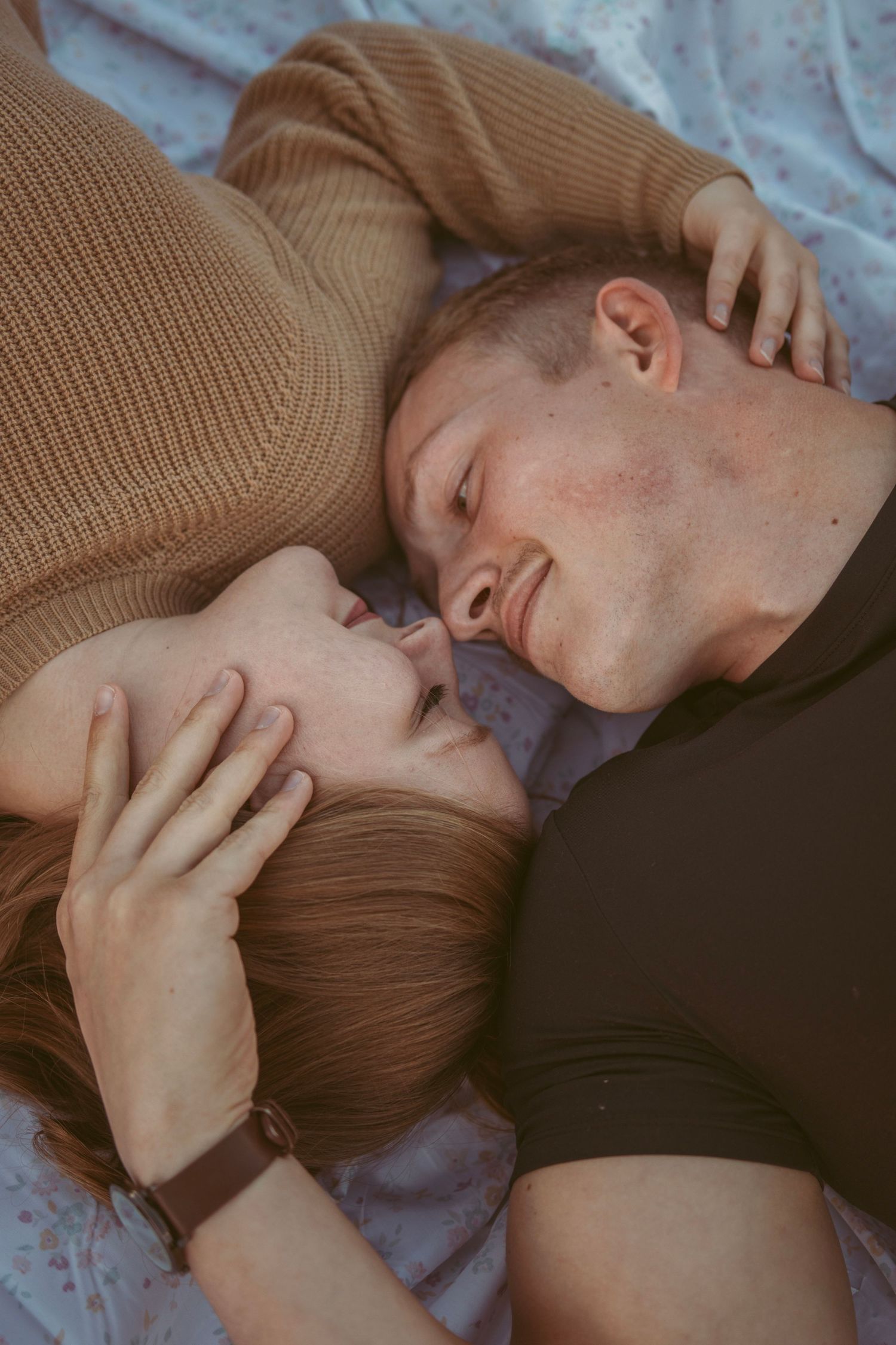 Tender embrace between two people on floral patterned sheets.