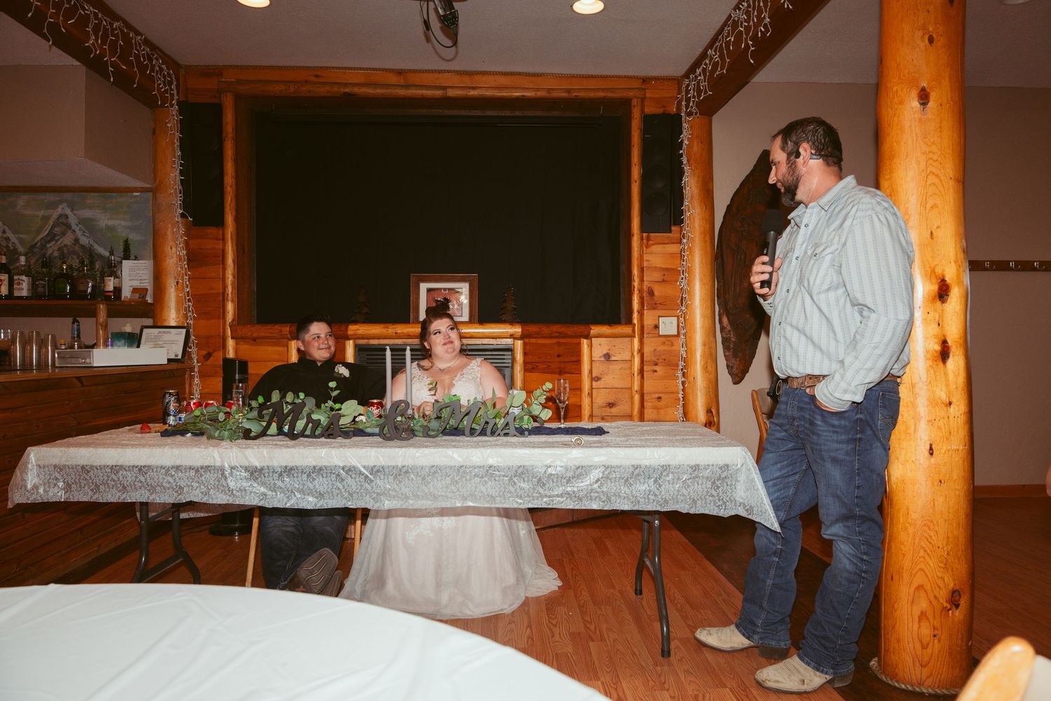 Wedding reception inside a rustic wooden lodge with exposed beams and white tablecloths.