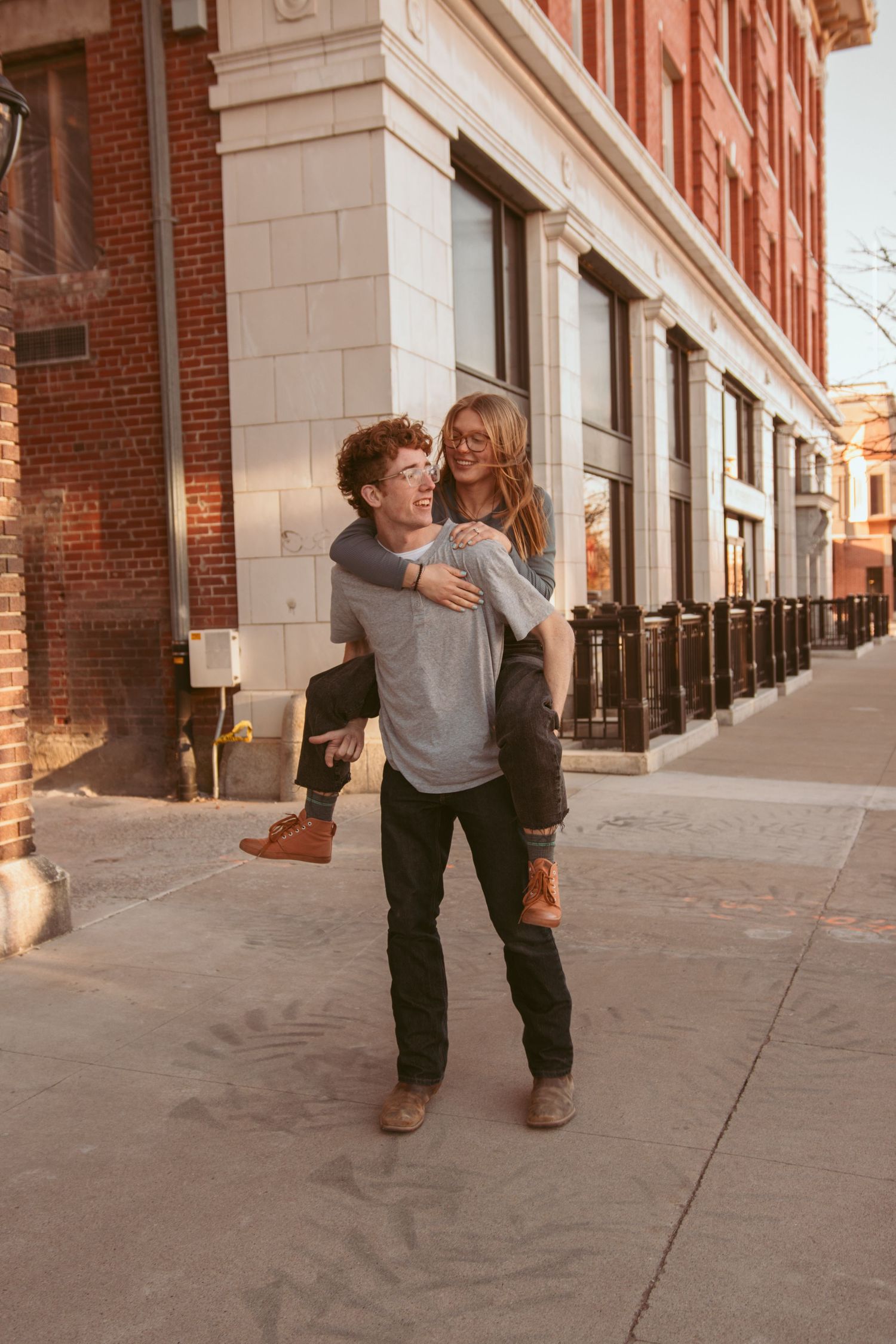 A couple playfully interacts and dances together along a brick building exterior.