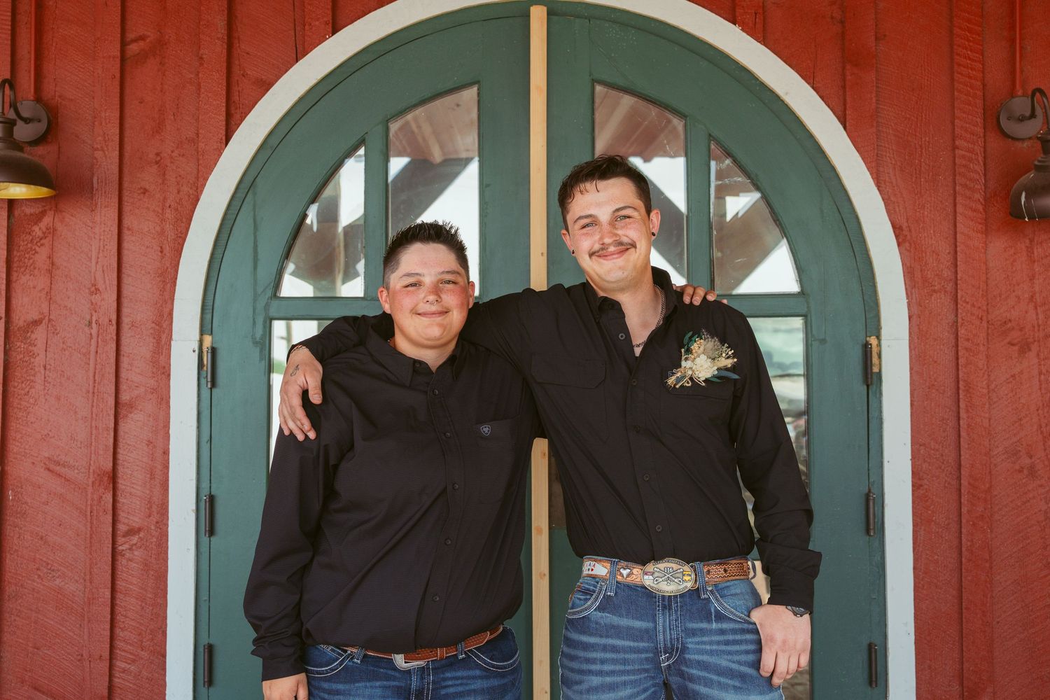 Wedding party poses casually in front of red building with arched teal doorways.