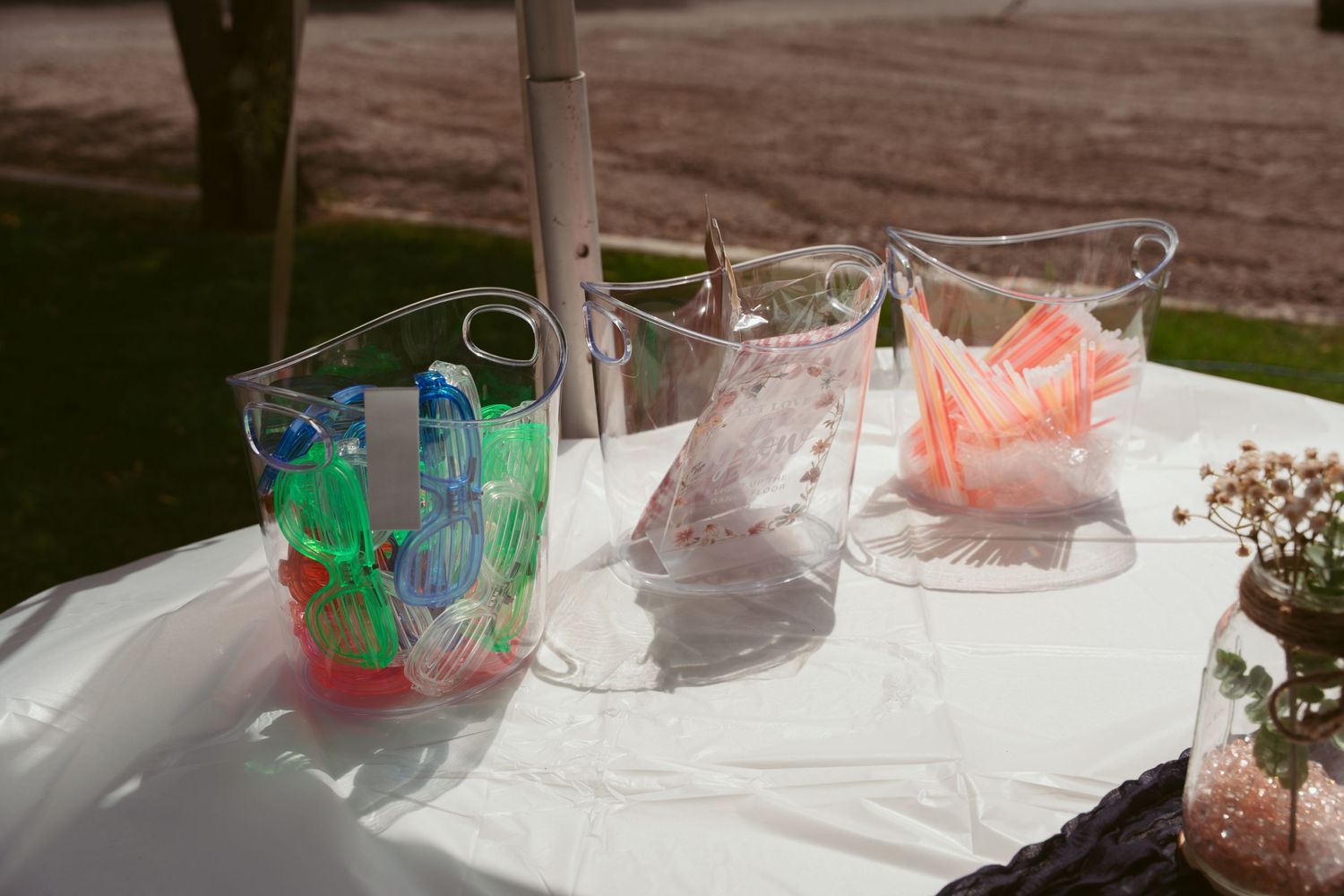 Clear glass containers and colorful party decorations arranged on a white table in sunlight.