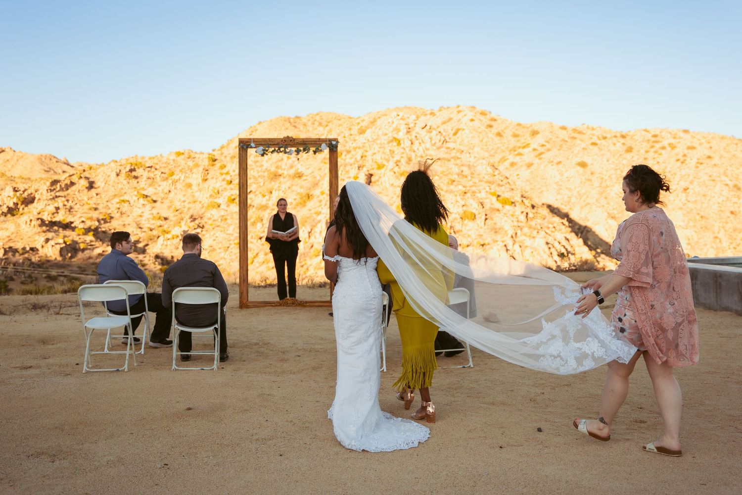 Wedding veil flowing in wind during desert ceremony with mountains in background.