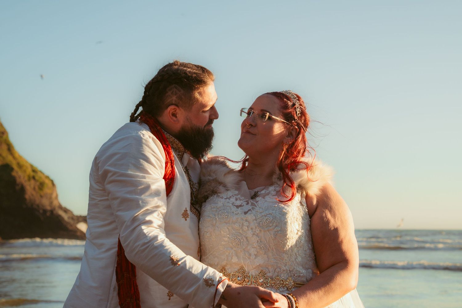 Intimate beachside moment captured during sunset with coastal cliffs in background.