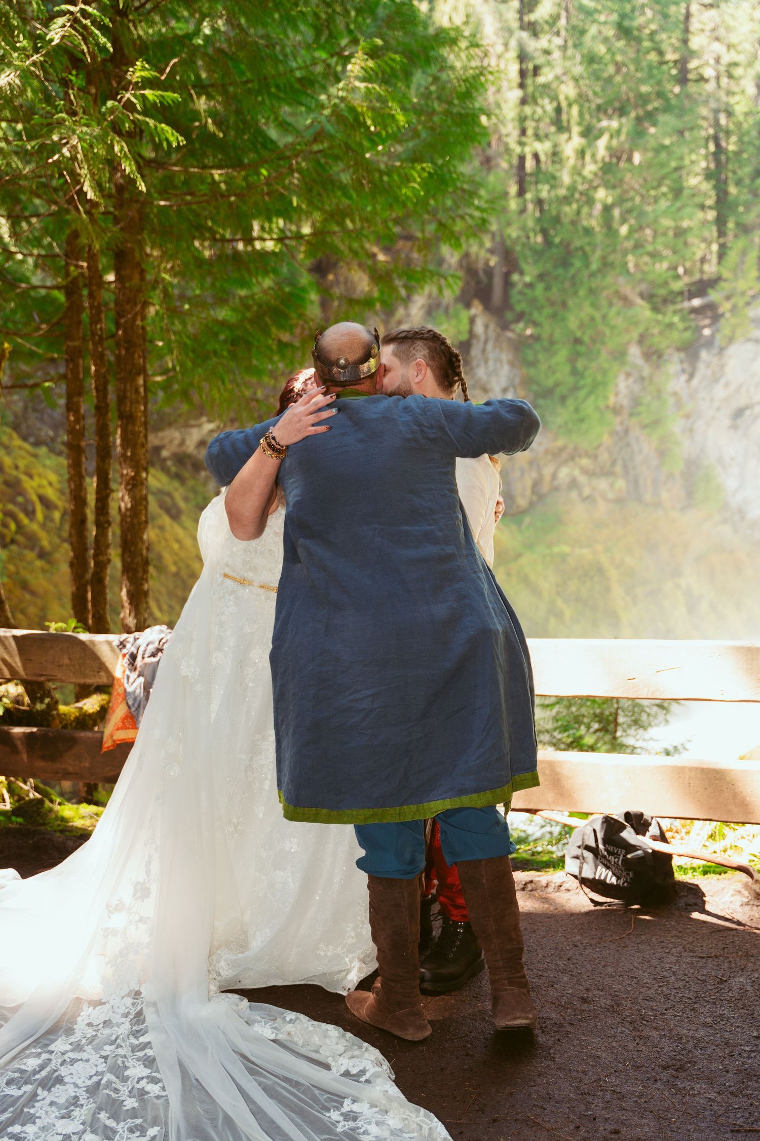 An emotional embrace during a forest wedding ceremony with a waterfall backdrop.