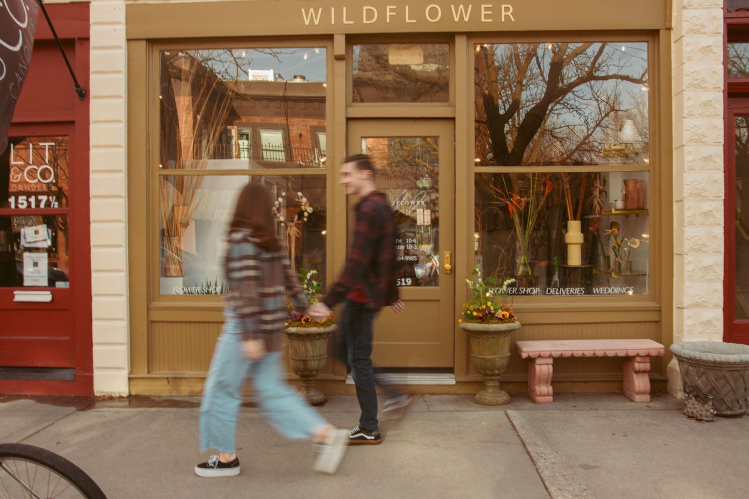 Two people walk past a storefront with 'Wildflower' signage and large windows on a city street.