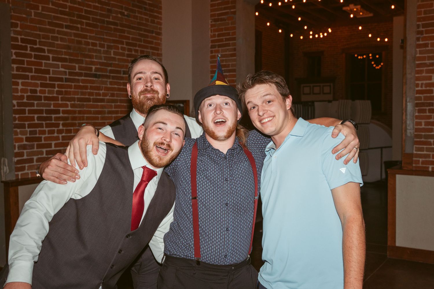 Wedding party members posing together in formal attire at a brick venue.