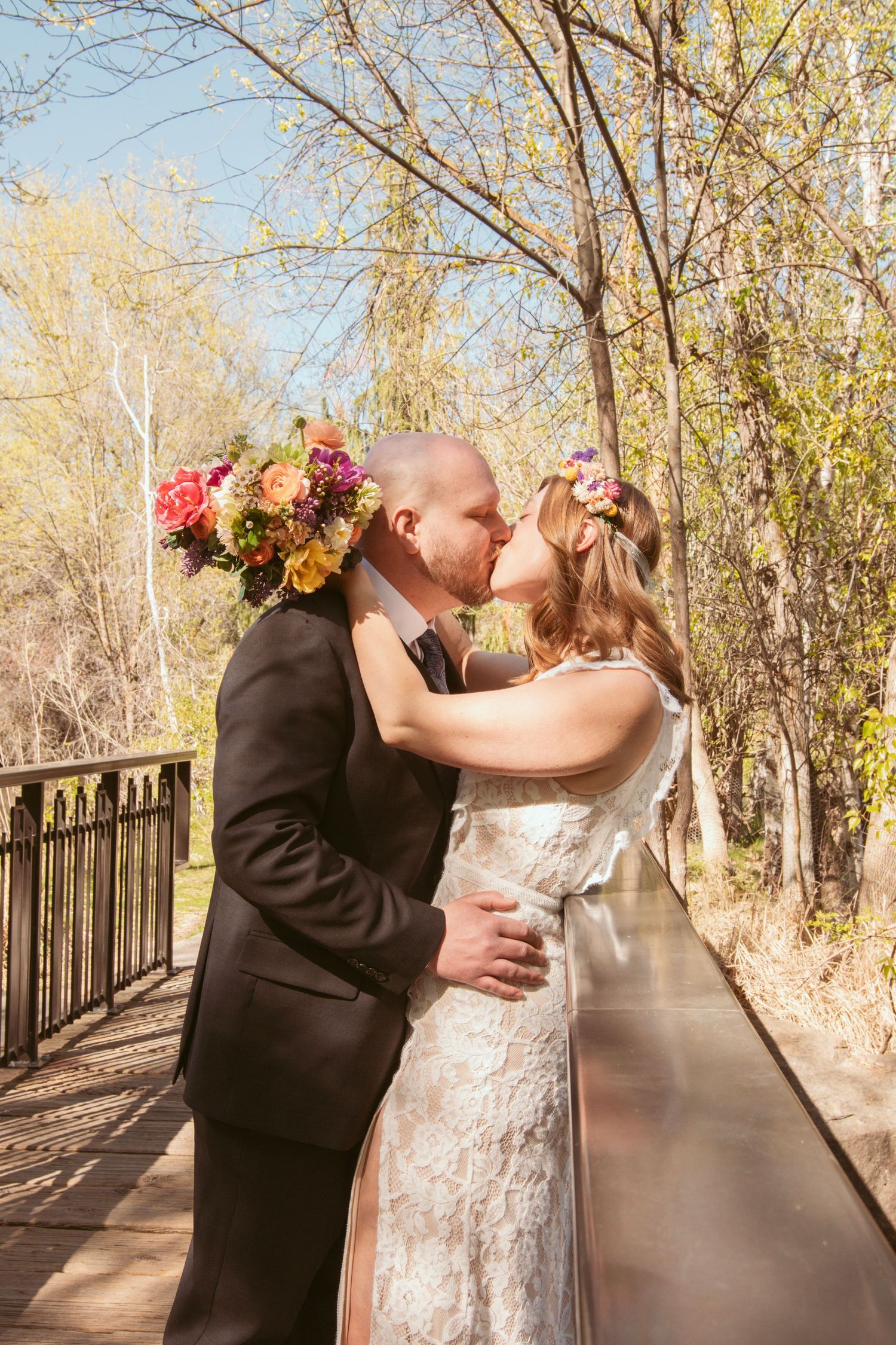 A romantic wedding couple kisses on a wooden bridge surrounded by autumn trees.