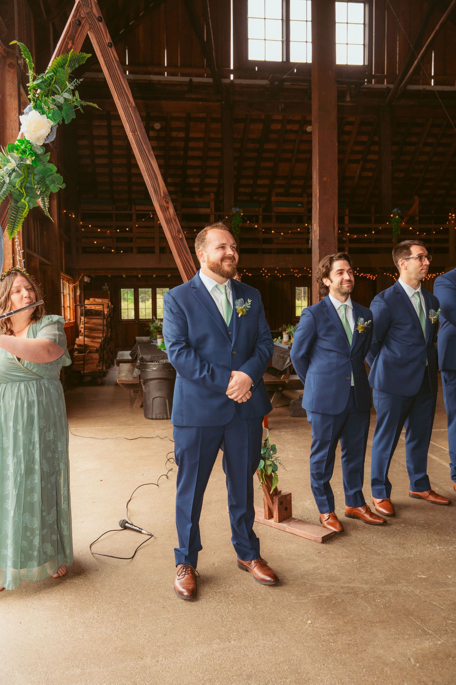 Groomsmen in matching navy suits and brown shoes line up inside rustic barn setting.